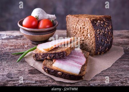 Tradizionali ucraine sandwich fatti di marrone pane di segale e lardo affumicato su un pezzo di carta marrone e legno naturale superficie testurizzata con unfocused Foto Stock