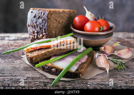 Tradizionali ucraine sandwich fatti di marrone pane di segale e lardo affumicato su un pezzo di carta marrone e legno naturale superficie testurizzata con unfocused Foto Stock