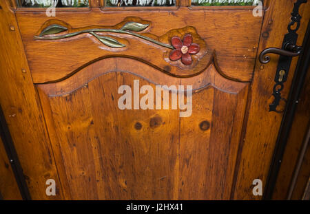 Primo piano di un fiore intagliato nella porta di ingresso in legno in stile cottage casa di tronchi. Foto Stock