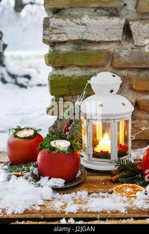 Lanterna bianca nel giardino d'inverno, mele, abeti e neve sul banco di legno. Foto Stock