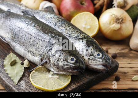 Due trote arcobaleno su tavola in legno rustico tra erbe e verdure. Cibo sano Foto Stock