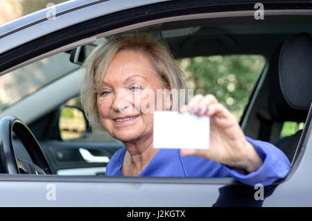 Donna anziana appoggiata attraverso la finestra aperta dal sedile di guida di una vettura che mostra la sua licenza con un felice sorriso amichevole Foto Stock