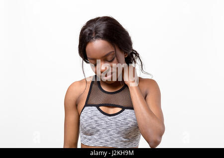 Stanchezza muscolare di giovane donna africana in un reggiseno per lo sport in piedi strofinando il collo per alleviare lo stress come si guarda verso il pavimento isolato su bianco Foto Stock