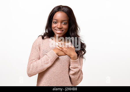 Giovane donna che mostra la sua sincera riconoscenza e gratitudine stringendo le mani al suo cuore con un sorriso soddisfatto Foto Stock