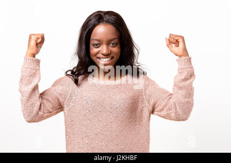 Esuberante esultante giovane donna africana tifo una vittoria, il successo o la punzonatura vincere l'aria con i suoi pugni e ridere su bianco con spazio di copia Foto Stock