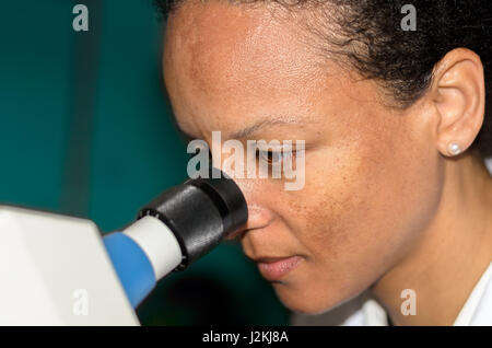 Vista laterale di una giovane donna africana mentre si osserva attraverso un microscopio Foto Stock