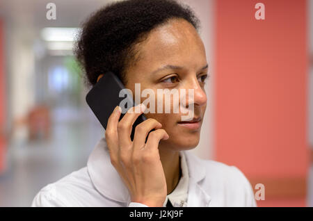 Grave giovane femmina medico a parlare su un telefono cellulare mentre si ascolta la conversazione in piedi in un ospedale Foto Stock