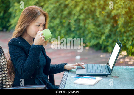 Business donna moderna con informazioni controllare dal laptop e bere un caffè la mattina. Foto Stock