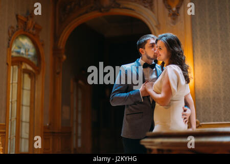 Bella sposi abbracciando e baciando balaustra vicino a splendide scale di antiquariato con lo sfondo del royal vintage in legno interno Foto Stock