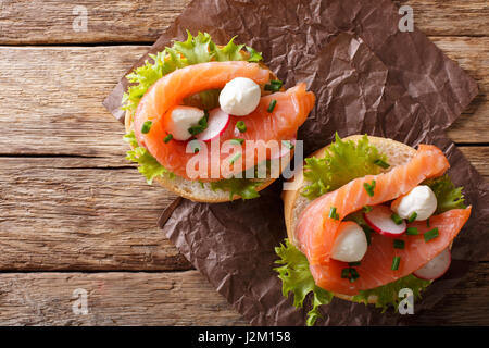 Panini con salmone salato, mozzarella, frisee, cipolla e ravanelli vicino sul tavolo. vista orizzontale dal di sopra Foto Stock