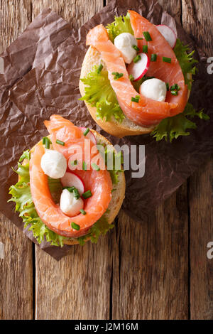 Panini con salmone salato, mozzarella, frisee, cipolla e ravanelli vicino sul tavolo. Vista verticale da sopra Foto Stock