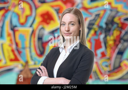 Fiducioso grinning donna bionda in maglione e camicia bianca con bracci ripiegati. Coloratissimo graffito arte in background. Foto Stock