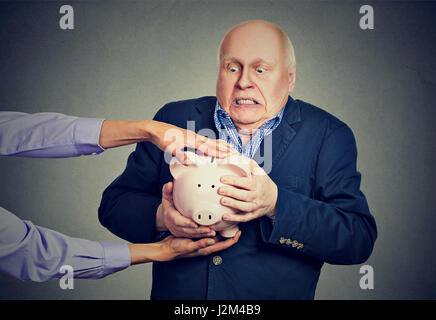 Anziani sconvolto spaventata business man holding salvadanaio cercando di proteggere i suoi risparmi vengano rubati isolato sfondo grigio Foto Stock