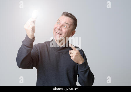 Motivati uomo di mezza età in possesso di una luminosa incandescente lampadina con uno sguardo di meraviglia gleeful concettuale del avente una brillante idea, rivoluzionario, in Foto Stock