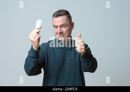 Motivati uomo di mezza età in possesso di una luminosa incandescente lampadina con uno sguardo di meraviglia gleeful concettuale del avente una brillante idea, rivoluzionario, in Foto Stock