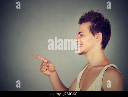 Guarda là! Felice giovane puntando con il dito a qualcuno o qualcosa in piedi contro lo sfondo grigio Foto Stock