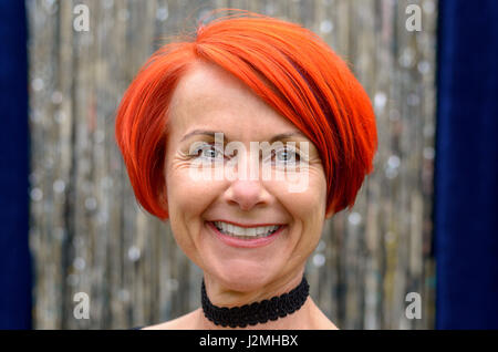 Attraente e vivace ed elegante redhead donna con un meraviglioso sorriso raggiante in posa davanti argentei orpelli natalizi in un vicino il colpo di testa Foto Stock
