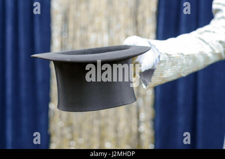 Gentleman o mago tenendo fuori un top hat nella sua mano nella parte anteriore di un azzurro sipario di un palcoscenico con festosa tinsel argento Foto Stock