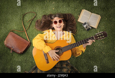 Hippy donna posa in erba e suonare la chitarra Foto Stock