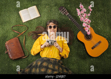 Hippy donna posa in erba accanto alla chitarra Foto Stock