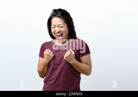 Esuberante esultante giovane donna cinese il tifo una vittoria, il successo o la punzonatura vincere l'aria con i suoi pugni e ridere su bianco con spazio di copia Foto Stock