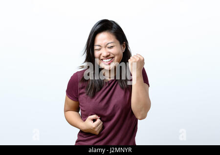 Esuberante esultante giovane donna cinese il tifo una vittoria, il successo o la punzonatura vincere l'aria con i suoi pugni e ridere su bianco con spazio di copia Foto Stock