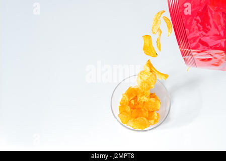Potato chips di cadere fuori un pacchetto di patatine in una ciotola di vetro bianco sul tavolo del lettino Foto Stock