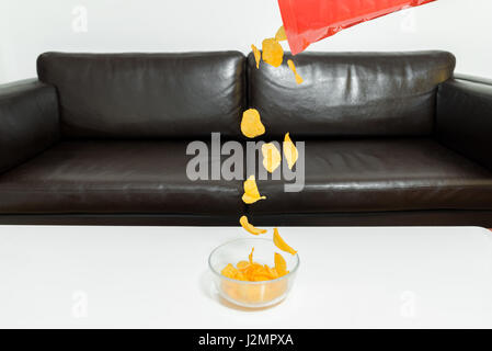Potato chips di cadere fuori un pacchetto di patatine in una ciotola di vetro bianco sul tavolo del lettino Foto Stock