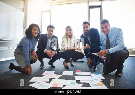 Sorridente team aziende con idee sparsi sul pavimento per ufficio Foto Stock