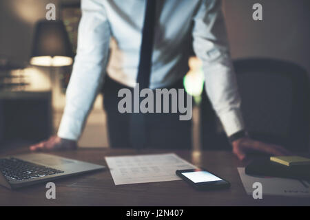 Il manager in piedi presso la scrivania e il sovraccarico di notte nel suo ufficio. Foto Stock