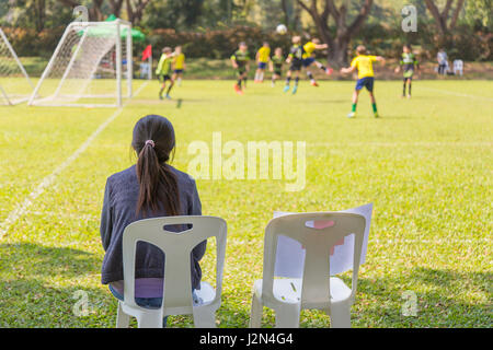 Donna guardando un ragazzo scuola di gioco del calcio in una giornata di sole Foto Stock