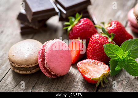 Macarons su un piatto di legno con fresca frutta di fragole e cioccolato Foto Stock