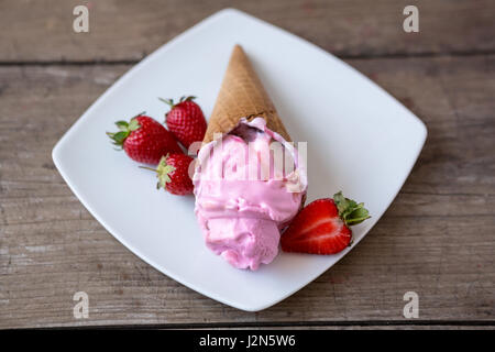 Gelato alla fragola nel cono di cialda sulla piastra Foto Stock