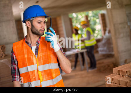 Uomo con casco e walky talky radio al sito in costruzione Foto Stock