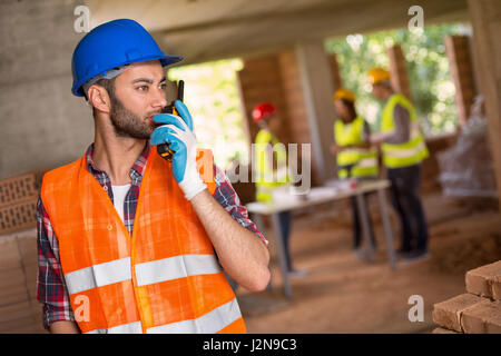 Uomo con casco e walky talky radio al sito in costruzione Foto Stock