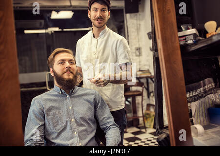 Sorridente barbiere maschio dando haircut client in negozio Foto Stock