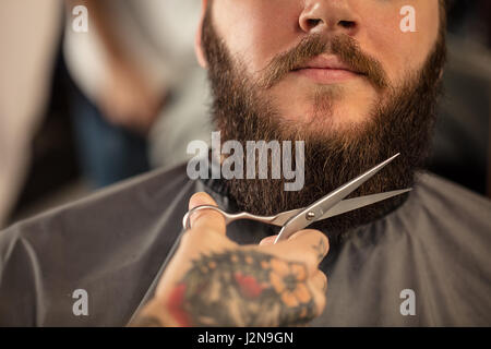 Barbiere con forbici per la rasatura uomo barbuto Foto Stock