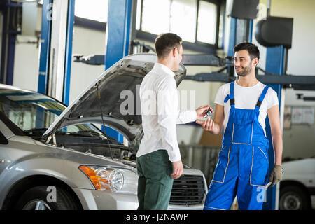 Il cliente dandogli le chiavi dell'auto a meccanica in servizio Foto Stock