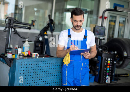 Meccanico maschio iscritto negli appunti nel negozio di riparazione Foto Stock