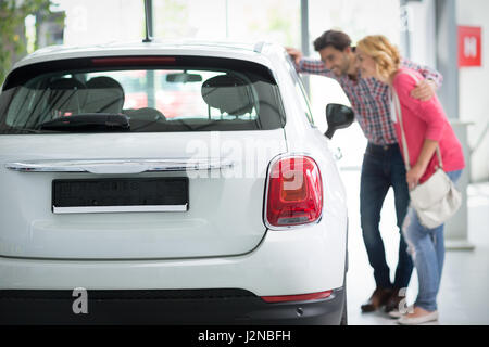 Bella coppia Giovane in piedi presso la concessionaria auto e rendendo la loro decisione, concetto acquistare nuove auto Foto Stock