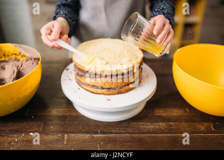 Donna cook mani versa la torta con lo sciroppo di zucchero. Gustosi dessert fatti in casa per la cottura Foto Stock