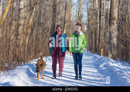Una madre e figlia a piedi il loro cane su una soleggiata giornata invernale. Foto Stock