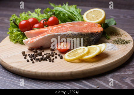 Materie filetti di salmone sul tagliere in legno. Foglie di lattuga, spezie, le fette di limone su una tavola di legno. Sfondo di Woody. Foto Stock