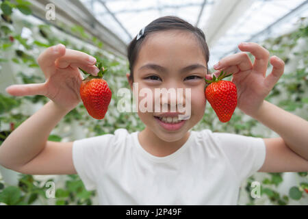 Felice ragazza asiatica holding fragole rosso in ogni mano Foto Stock