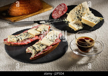 Due panini da pane nero con formaggio di Dorblu e materie salsiccia affumicata sul tondo nero ardesia piastre, un coltello per formaggio, un tagliere di legno con Foto Stock