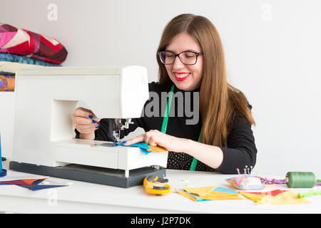 Ricamo e la trapuntatura in officina di una giovane donna - vicino a femmina sarto lavora con una macchina da cucire e fili, tessuti, aghi, spilli, pulsanti. Foto Stock