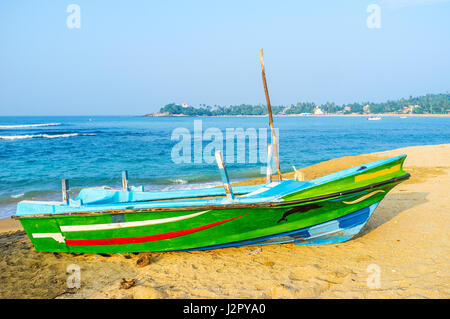 La colorata barca sulla sabbia di unawatuna beach con la vista su unawatuna devol devalaya tempio sulla distanza, sri lanka. Foto Stock