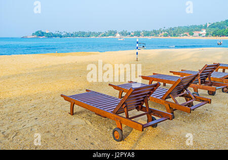 La fila di lettini in legno sulla sabbia della spiaggia di Unawatuna, Sri Lanka. Foto Stock