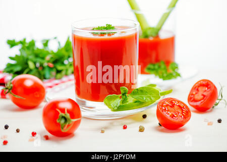 Il succo di pomodoro in bicchieri di vegetazione, basilico, tagliato i frutti di pomodoro e tovagliolo sulla luce sullo sfondo di legno, concetto cibo vegetariano, close up Foto Stock