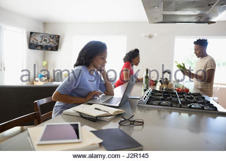 African American madre lavora al computer portatile e i figli adolescenti la cottura in cucina